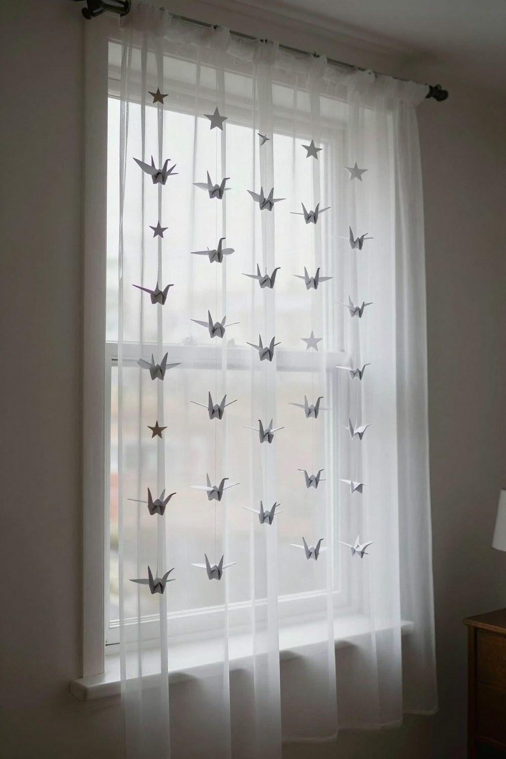 Garland of white origami cranes and stars hanging vertically by a window