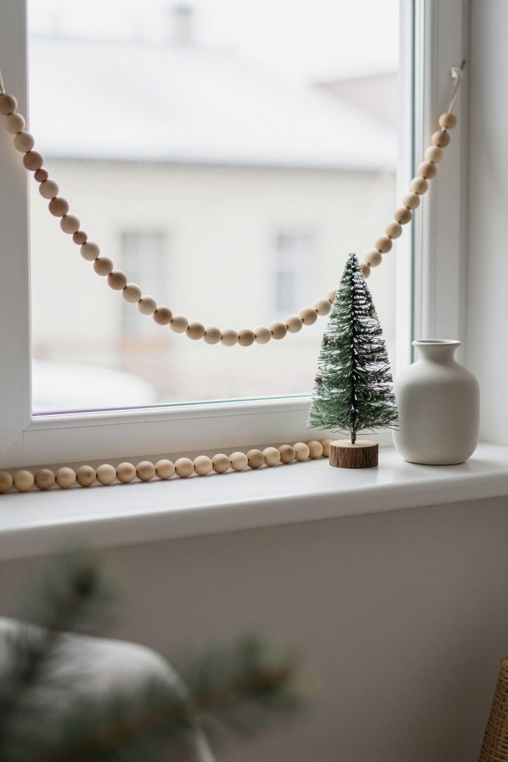 Wooden bead garland on a white shelf with a small tree and a ceramic vase