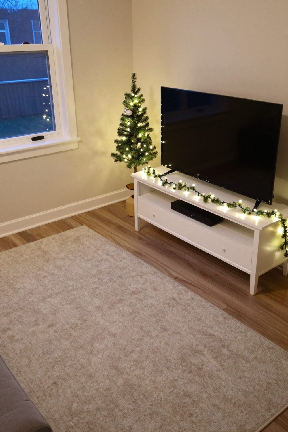 Small TV stand in an apartment with one small tree and a garland